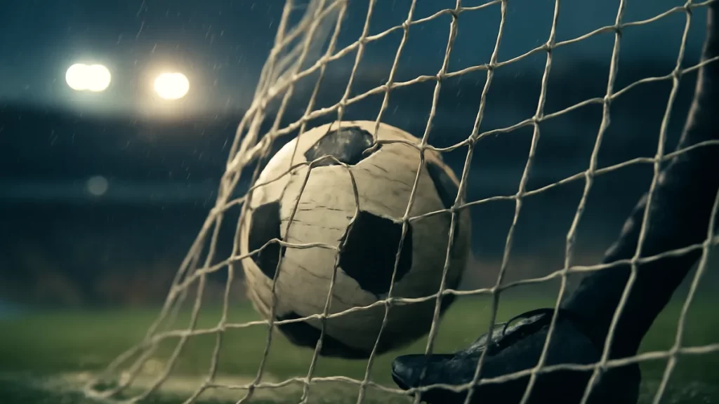 Football in net on rain-slick pitch, scuffed boots, blurred empty stands.
