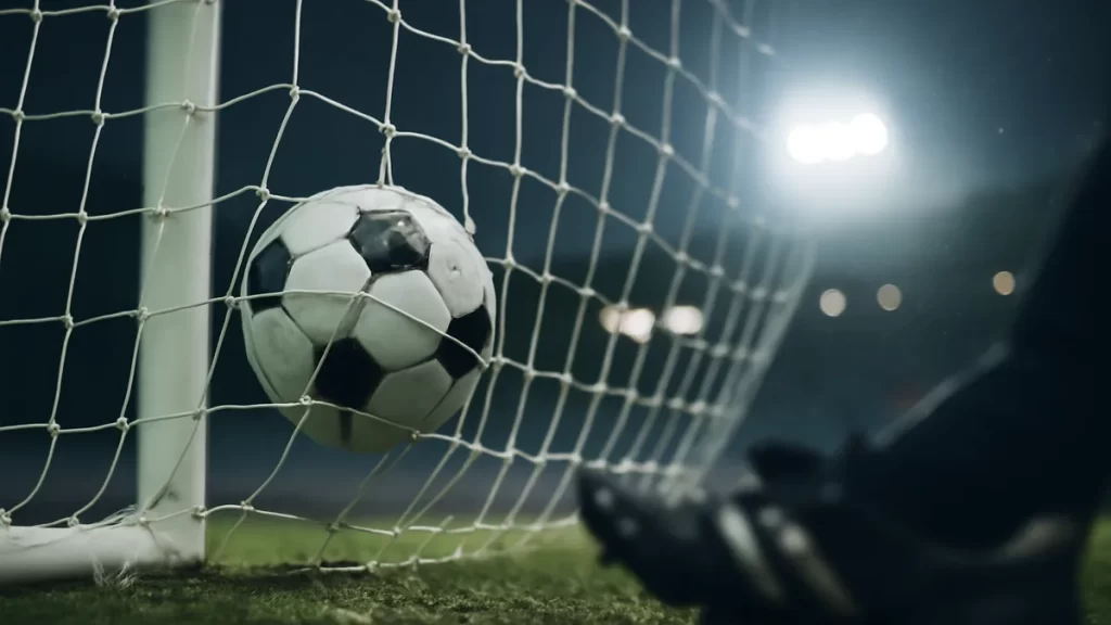 Holdt hat-trick sparks Tottenham’s seven-goal second-half blitz Football in net with boot foreground, floodlights and rainy empty stands.