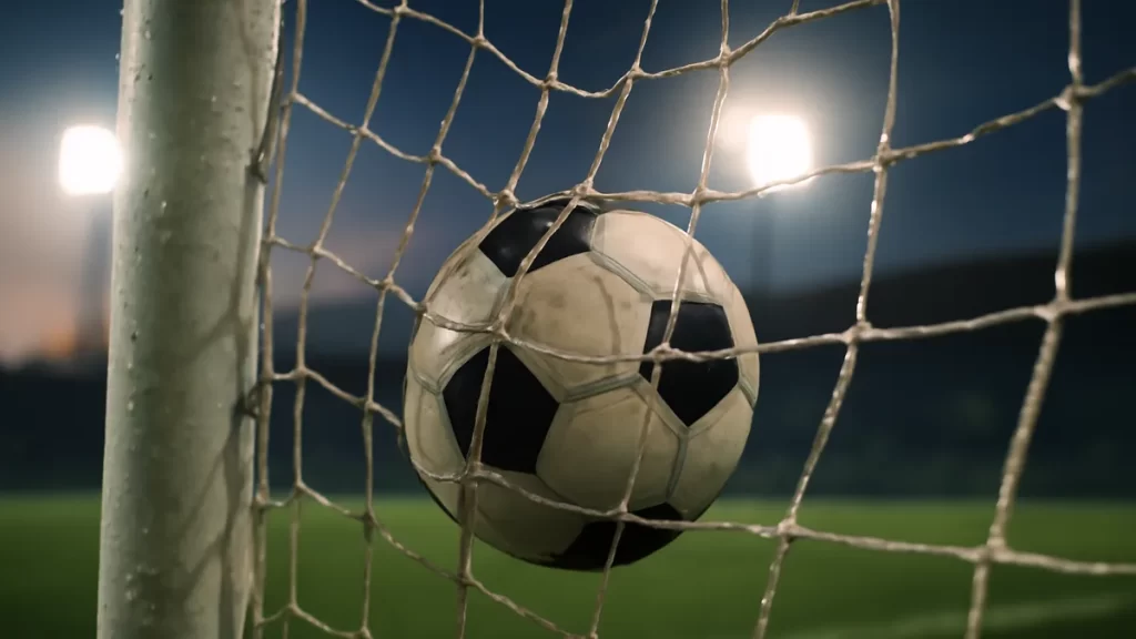 Football tangled in net at dusk with wet pitch and floodlights